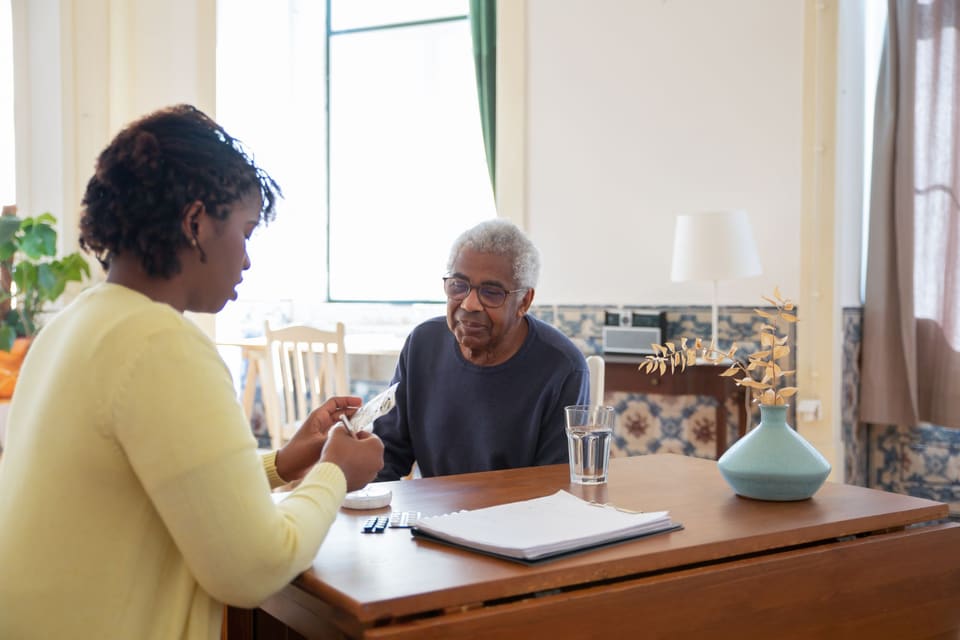 Begeleider bespreekt papieren met een oudere man aan de keukentafel