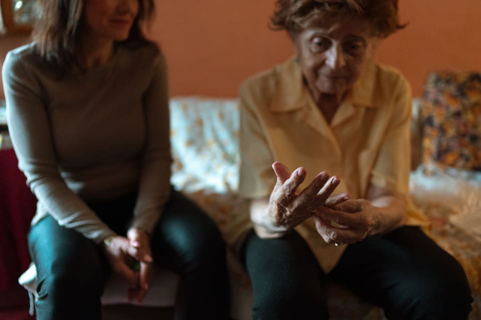 Zorgmedewerker in gesprek met een oudere vrouw op de bank